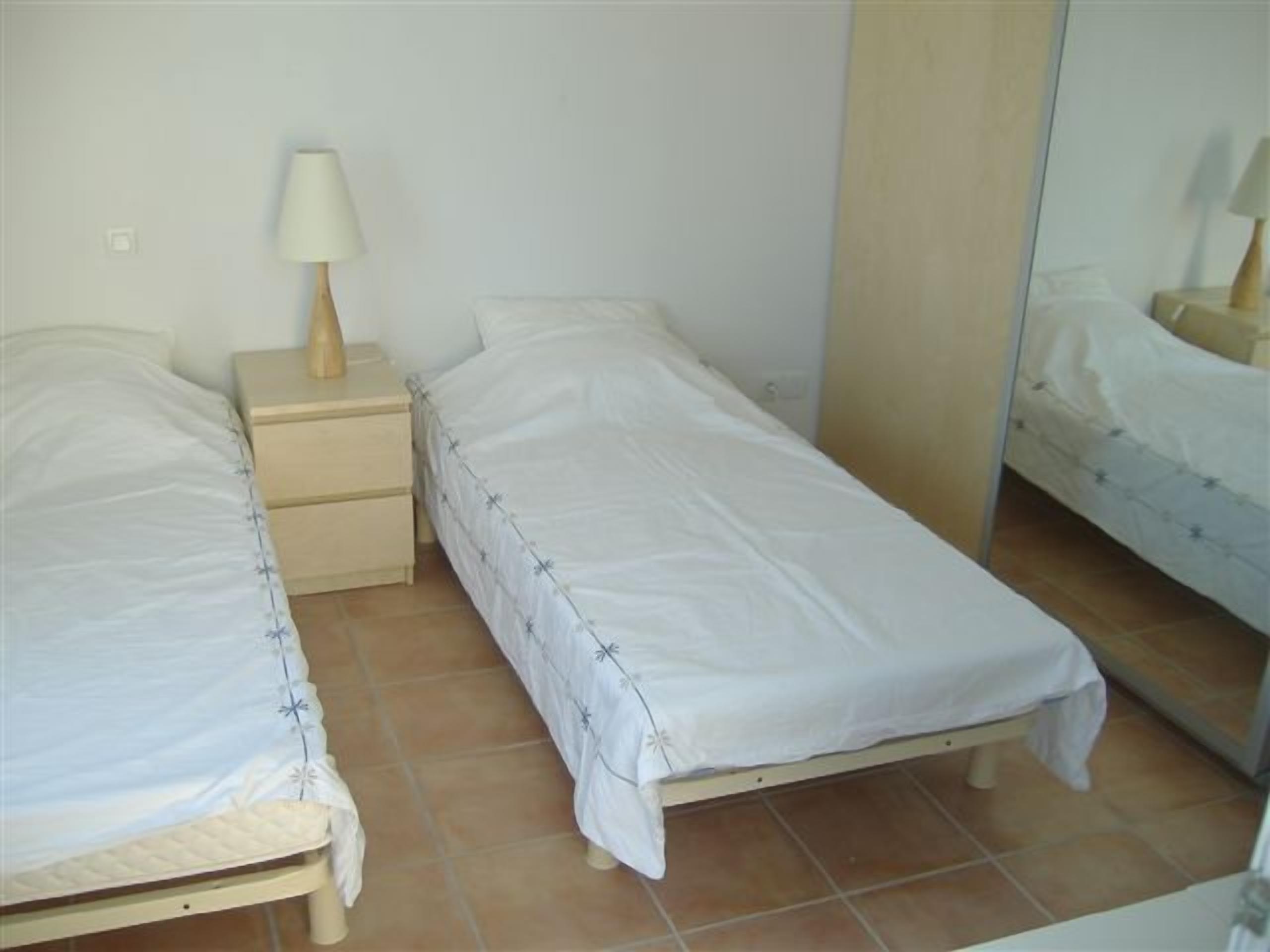Een kleine, schone kamer met twee eenpersoonsbedden, een nachtkastje met lamp en een grote spiegel.