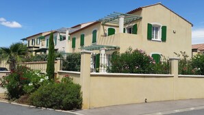 Ein zweistöckiges Gebäude mit grünen Fensterläden, einem Balkon und einem kleinen Garten mit Blumen.