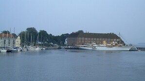A waterfront property with a large building, a marina with several boats, and a calm sea.