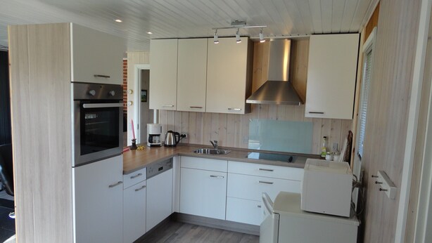 A modern kitchen with white cabinets, a stainless steel range hood, and a built-in oven.