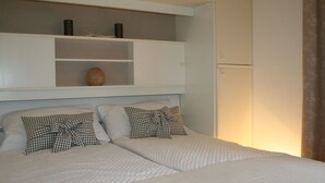 A bedroom with two beds, a white headboard, a shelf with decorative items, and a wall-mounted refrigerator. - 1A apartment, 2-4 people, very close to the beach, central, large garage, family friendly (Sylt)