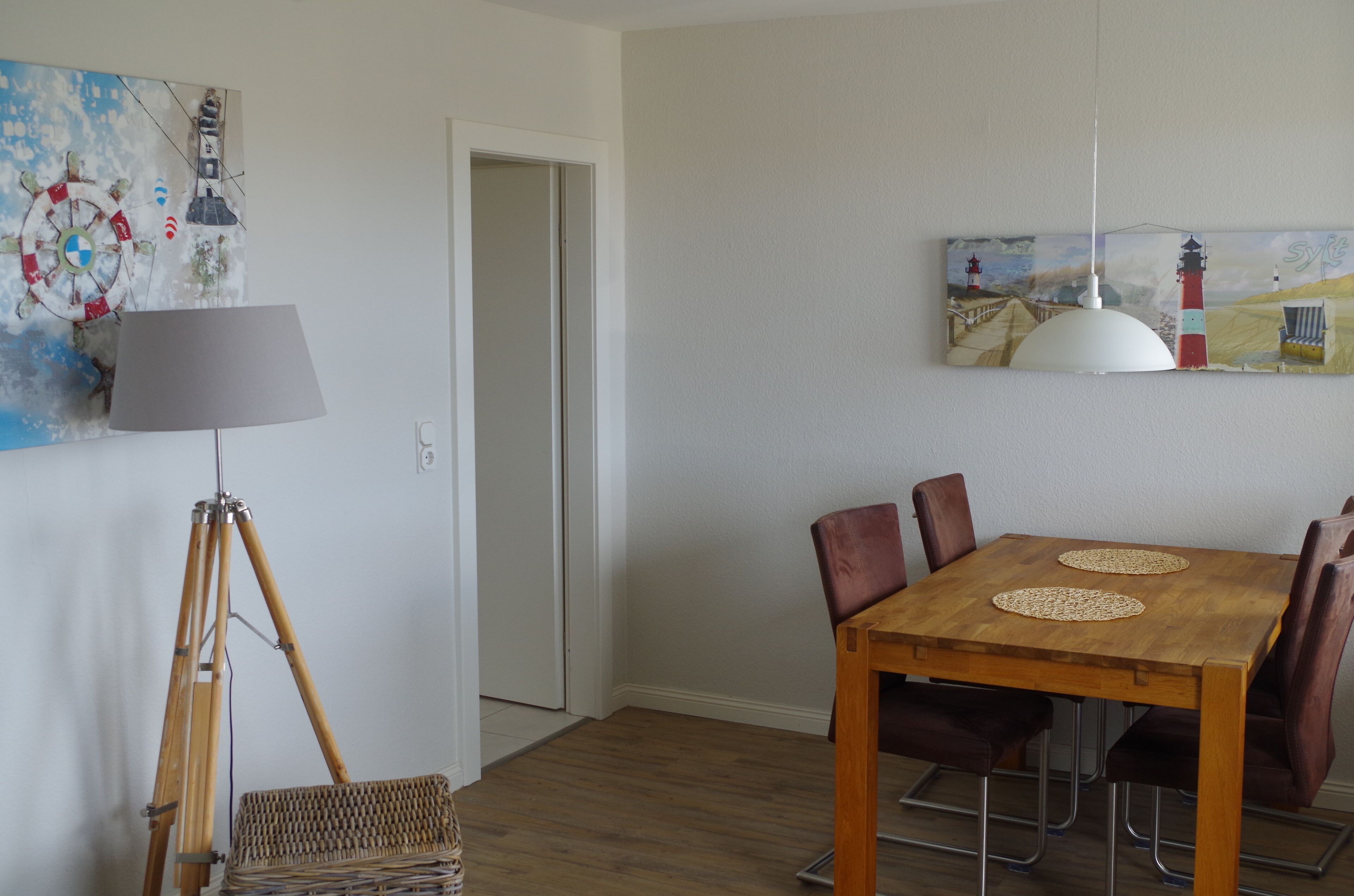 A dining area with a wooden table, chairs, a lamp, and artwork on the walls.
