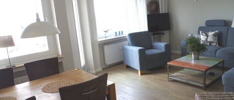 A modern living room with a dining area, a blue sofa, a television, and a large window.