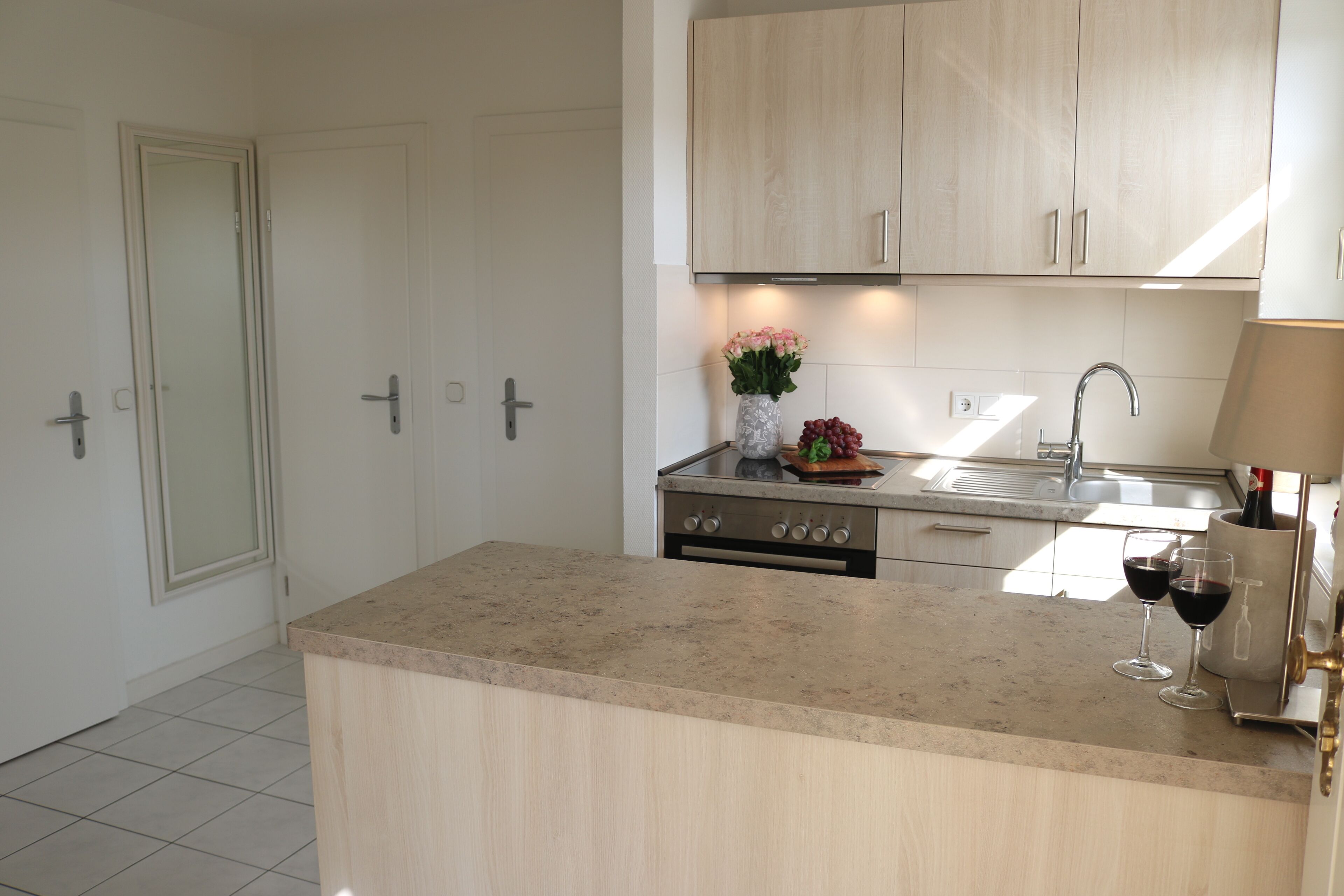 A modern kitchen with light wood cabinets, a central island, and a built-in oven.