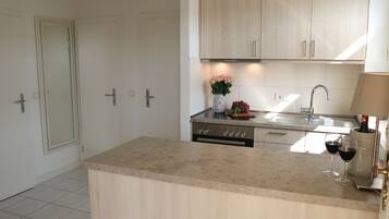 A modern kitchen with light wood cabinets, a central island, and a built-in oven.