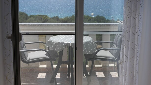 A balcony with a table and chairs, overlooking a body of water and distant hills.