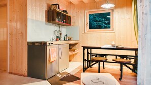 A wooden interior with a kitchenette, a dining table with chairs, and a framed picture on the wall.
