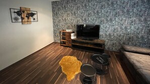 Een moderne woonkamer met een flatscreen televisie op een houten standaard, een wereldkaart als kunstwerk aan de muur, en behang met een patroon.