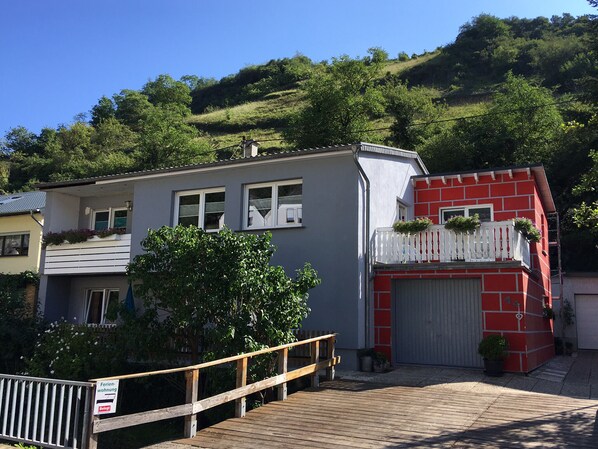 Ein zweistöckiges Gebäude mit einer grauen Fassade, einem roten Abschnitt mit einem weißen Balkon und einer hölzernen Veranda.