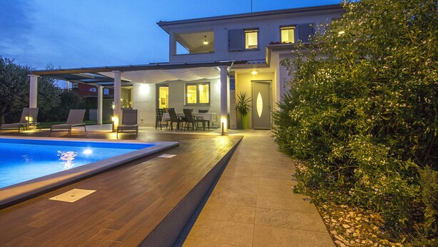 Une maison moderne dotée d’une piscine, d’un espace salon extérieur et d’une terrasse bien éclairée.