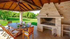 Une terrasse extérieure avec un barbecue en pierre, une table en bois et des chaises.