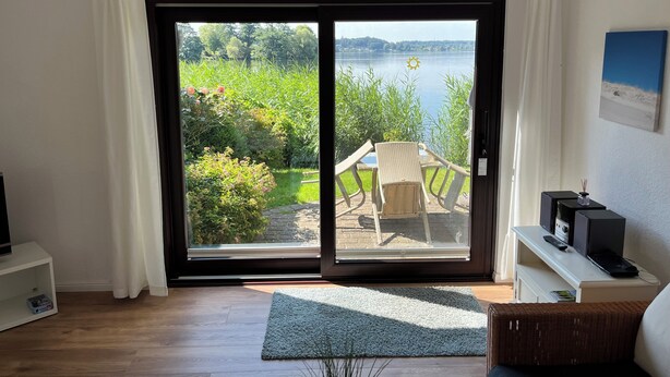 Et værelse med en skydedør til en have med et bord og stole, et hvidt konsolbord med en højttaler og fjernbetjening, samt et fjernsyn på et stativ.