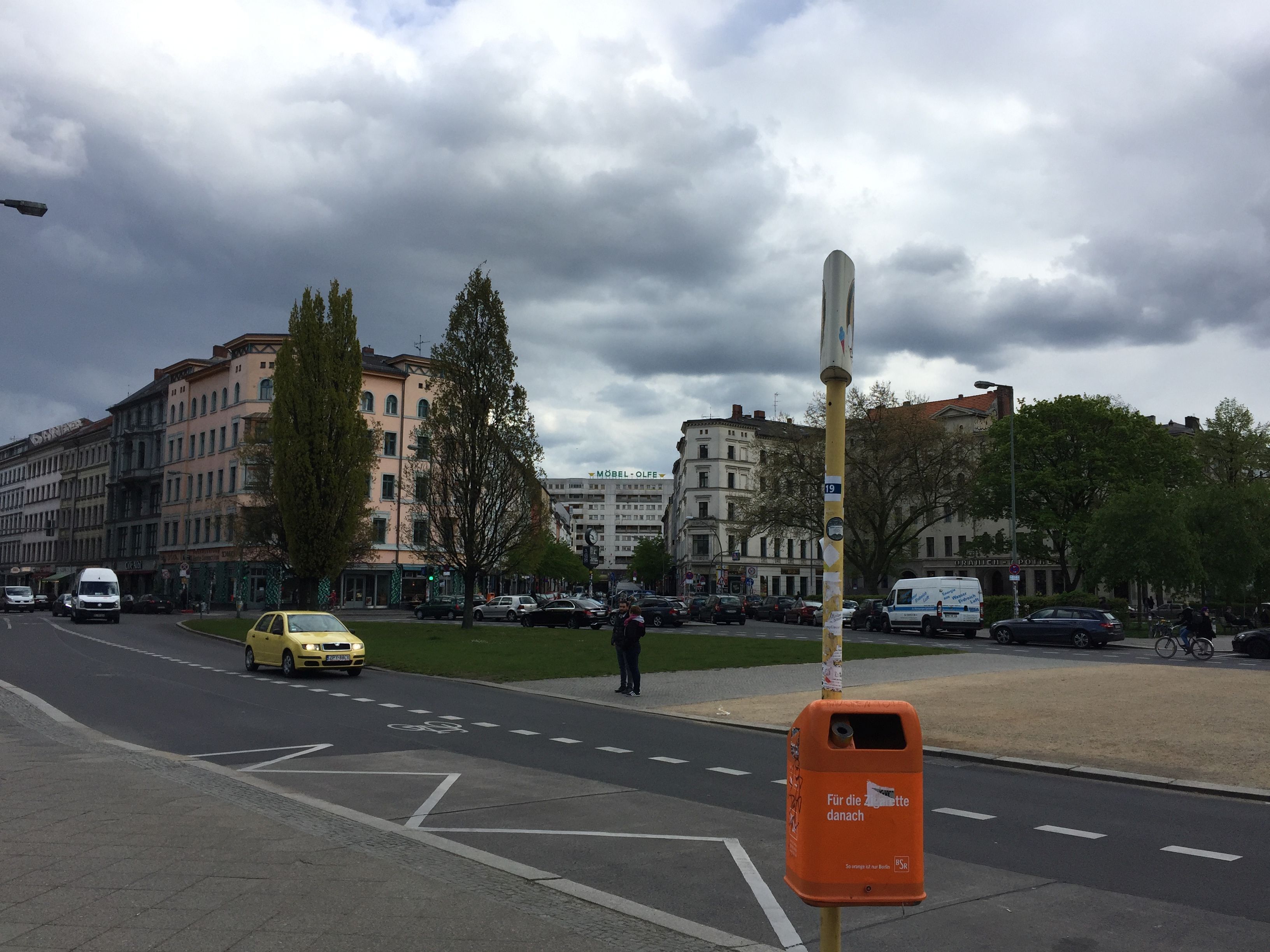 A street with buildings, a yellow taxi, and a mailbox.