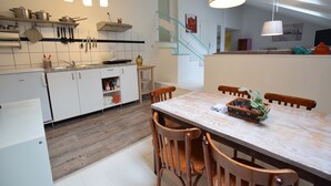 Moderni keittiö, jossa on valkoiset kaapit, puinen ruokapöytä ja riippuvalaisimet.
