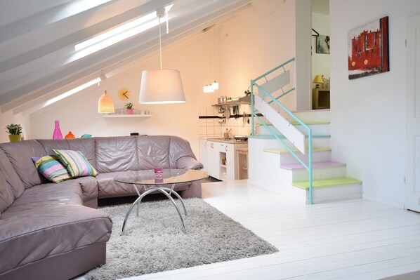 A modern living room with a leather sofa, a glass coffee table, and a staircase with colorful steps.