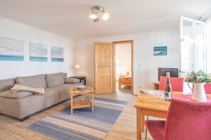 Een woonkamer met een bank, een salontafel en een eettafel met stoelen. Er is een houten deur die naar een andere kamer leidt.