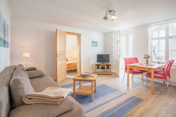 A living room with a sofa, a coffee table, a TV, and a dining area with a table and chairs. - Apartment 3 - HausSeebär (Heringsdorf)