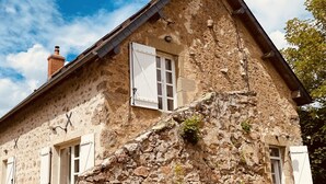 A rustic stone house with a steeply pitched roof, white shutters, and a chimney.