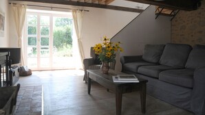 A living room with a sofa, a coffee table with a vase of flowers, a fireplace, and a view through a glass door to the outside.