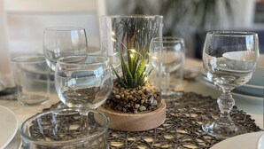 Une table à manger avec de la vaisselle en verre transparent, une petite plante en pot et un set de table en fibres tressées.