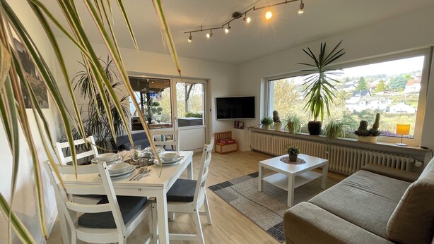 Un salon moderne comprenant un coin repas, un canapé et une grande fenêtre donnant sur des maisons.