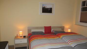 Ein Schlafzimmer mit einem Bett, zwei Nachttischen, einem Fenster und einem gerahmten Bild an der Wand.