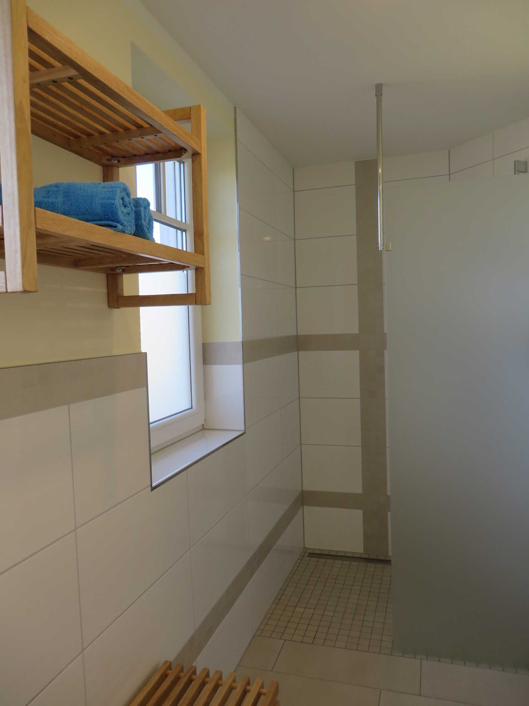 A bathroom with a shower, a window, and a wooden shelf with towels.