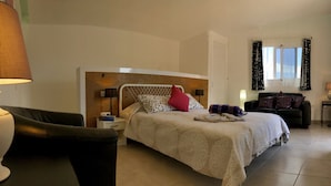 Une chambre à coucher avec un lit, des tables de chevet, une chaise, un canapé et une fenêtre avec des rideaux.