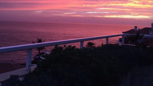 Un coucher de soleil sur l’océan, avec une rambarde au premier plan.
