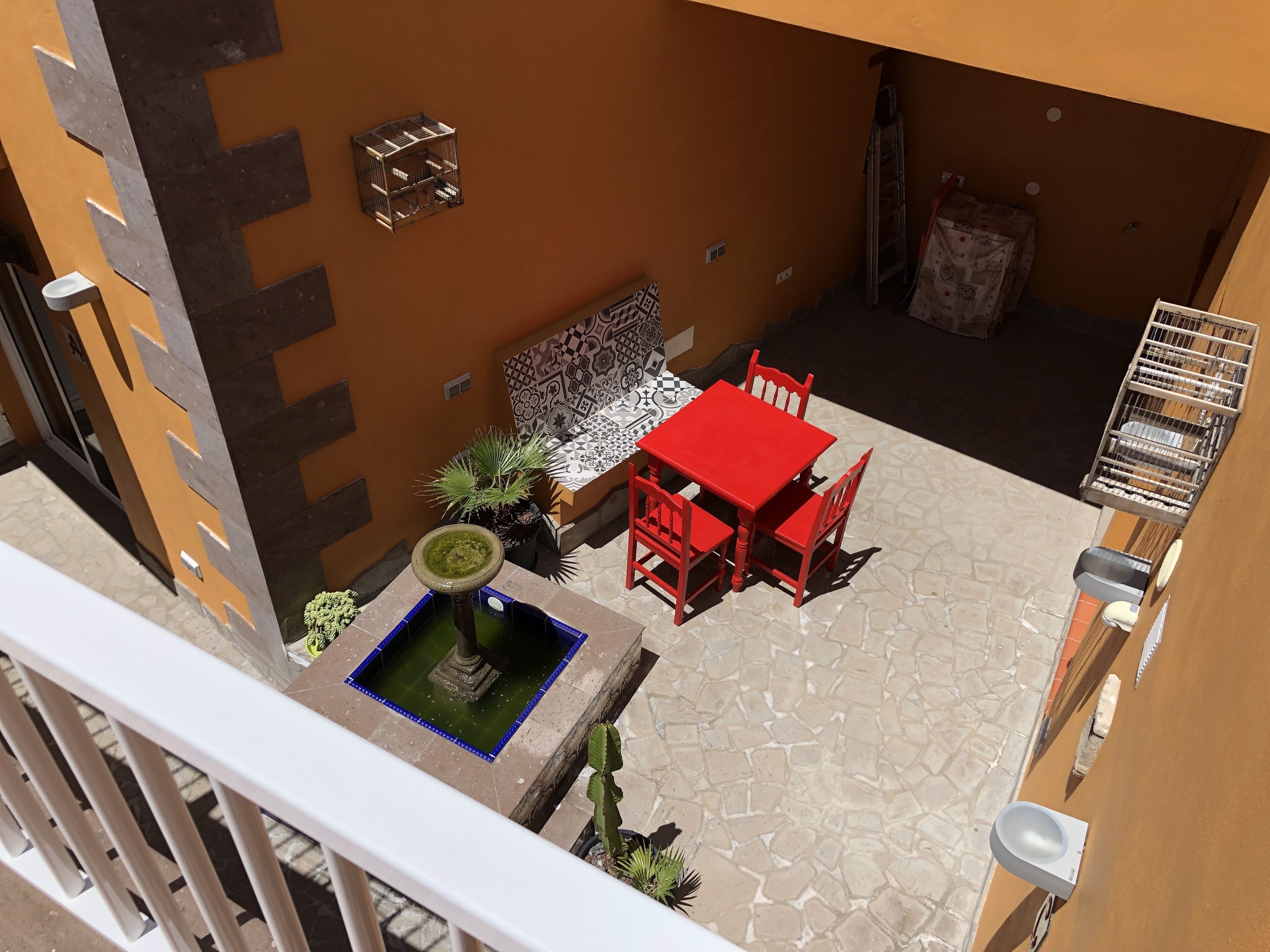 Un patio con una mesa y sillas rojas, una pequeña fuente y un muro con diseño.