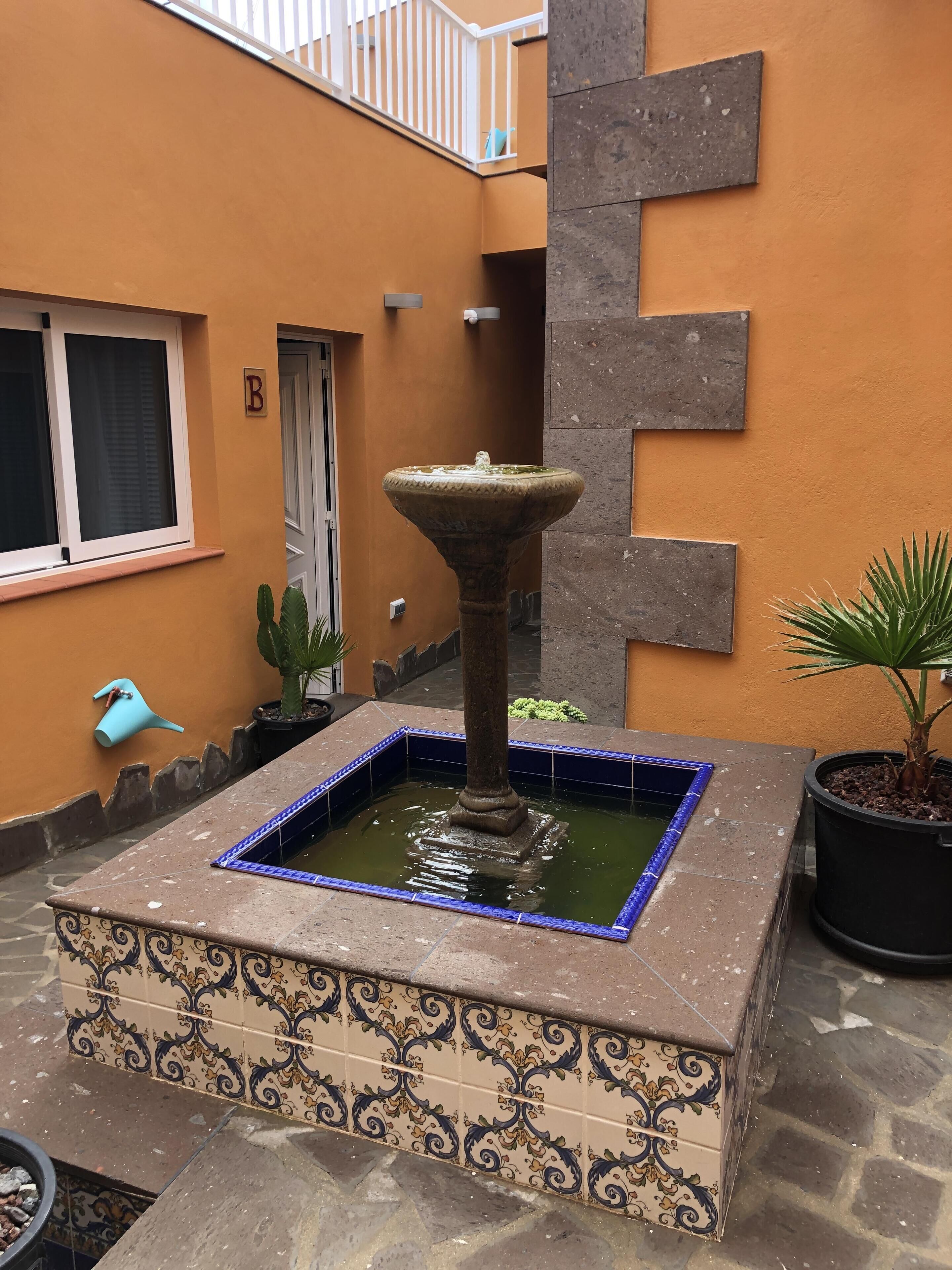 Une cour agrémentée d’une fontaine décorative, d’un pot de fleurs et d’un mur recouvert de carreaux.