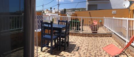 Une terrasse avec un sol carrelé, une table entourée de chaises et un fauteuil de jardin rouge.