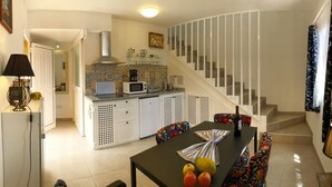 Une cuisine moderne avec des meubles blancs, un four à micro-ondes et une cuisinière à gaz. On y trouve un coin repas avec une table dressée pour deux personnes, ainsi qu’un escalier avec une rampe blanche menant à l’étage supérieur.