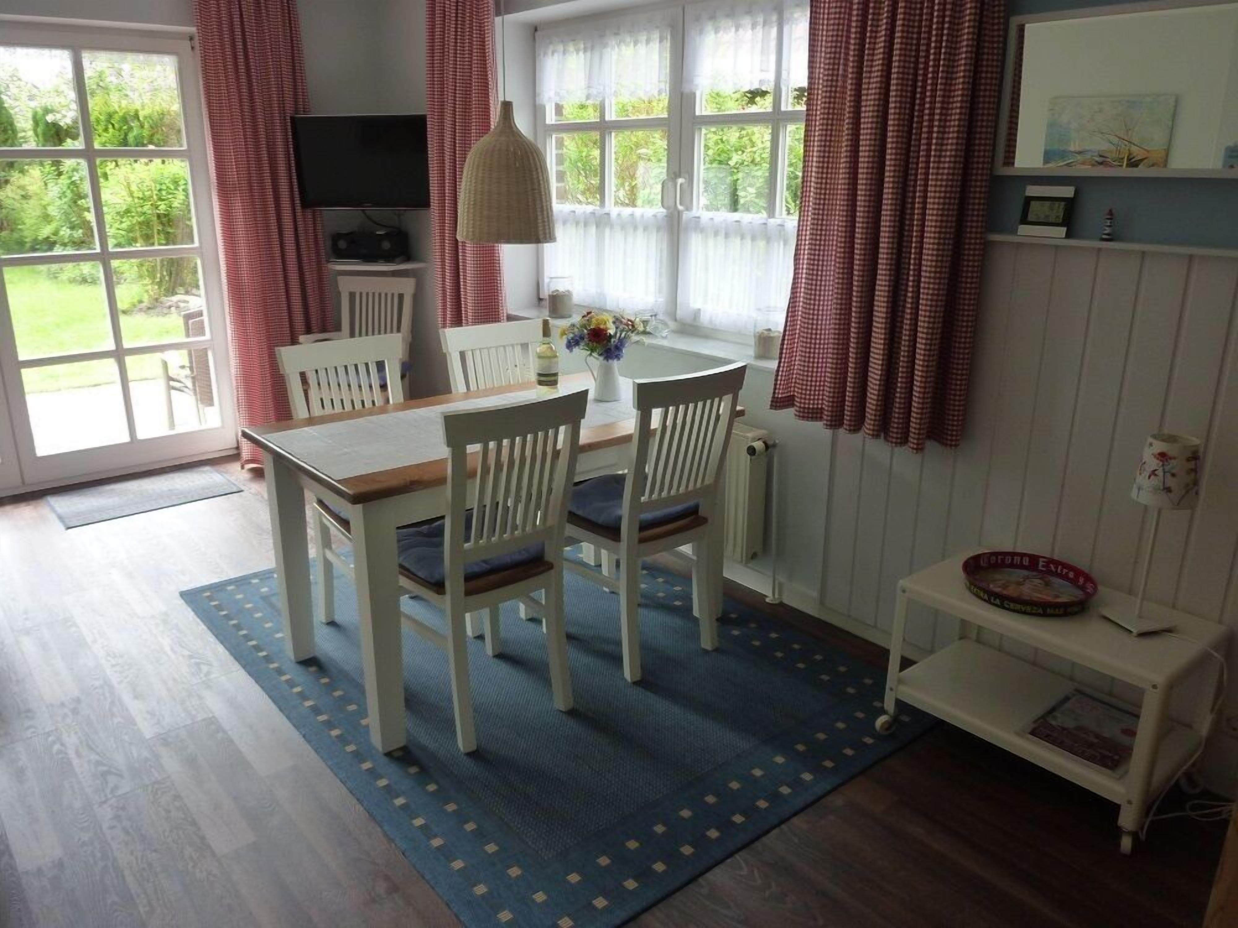 A dining area with a table and chairs, a television, and a window with curtains.