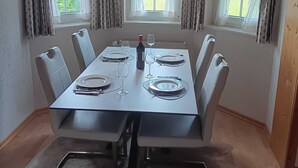 A dining area with a rectangular table set for six, flanked by two windows with curtains, a ceiling light, and a wooden ceiling. - Beautiful, large, comfortable vacation apartment to feel at home in. (Dachsberg (Südschwarzwald))