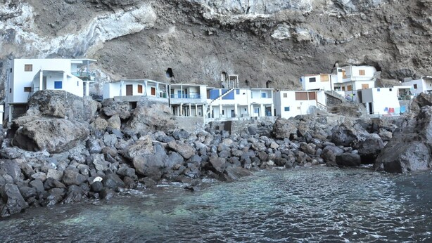 Un ensemble de bâtiments côtiers comprenant plusieurs structures blanches, dont certaines sont dotées de balcons, situé sur une côte rocheuse, avec une eau claire devant.