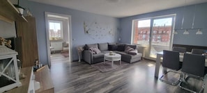 Ein modernes Wohnzimmer mit einem grauen Sofa, einem kleinen runden Couchtisch und einem Essbereich mit Tisch und Stühlen.