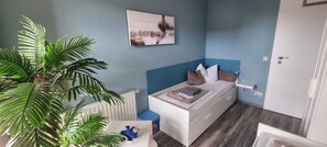 Un dormitorio con cama, radiador, pared azul, puerta y planta.