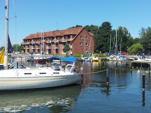 Eine Marina mit vertäuten Booten, ein Backsteinhaus mit Balkonen und ein klarer Himmel.