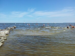 Una playa con gente nadando y barcos en el agua.