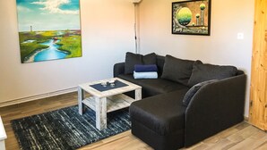 Una sala de estar con un sofá oscuro, una pequeña mesa de centro de madera y dos cuadros en la pared.