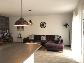 Una sala de estar moderna con un sofá modular, una mesa de centro, iluminación colgante, un reloj y una lámpara de pie.