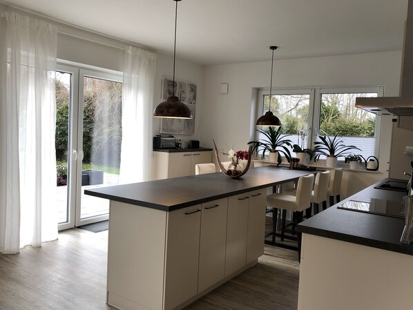 Una cocina moderna con una isla central, iluminación colgante y vistas al jardín a través de amplios ventanales.