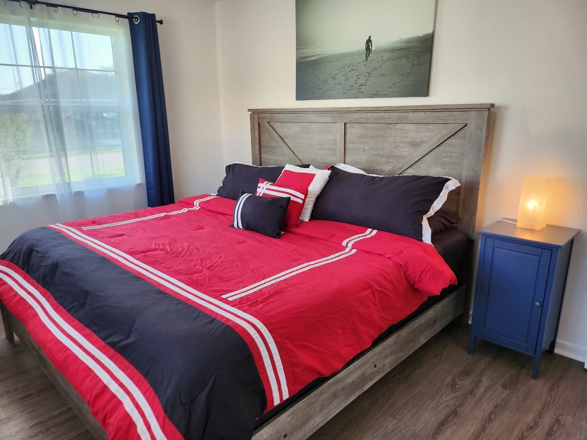 A bed with a red and black bedspread, a wooden headboard, and a bedside table with a lamp.