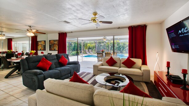 A spacious living area with a pool view, a dining area, and a TV mounted on the wall. - Holiday home with large heated pool - south exposure (Cape Coral)