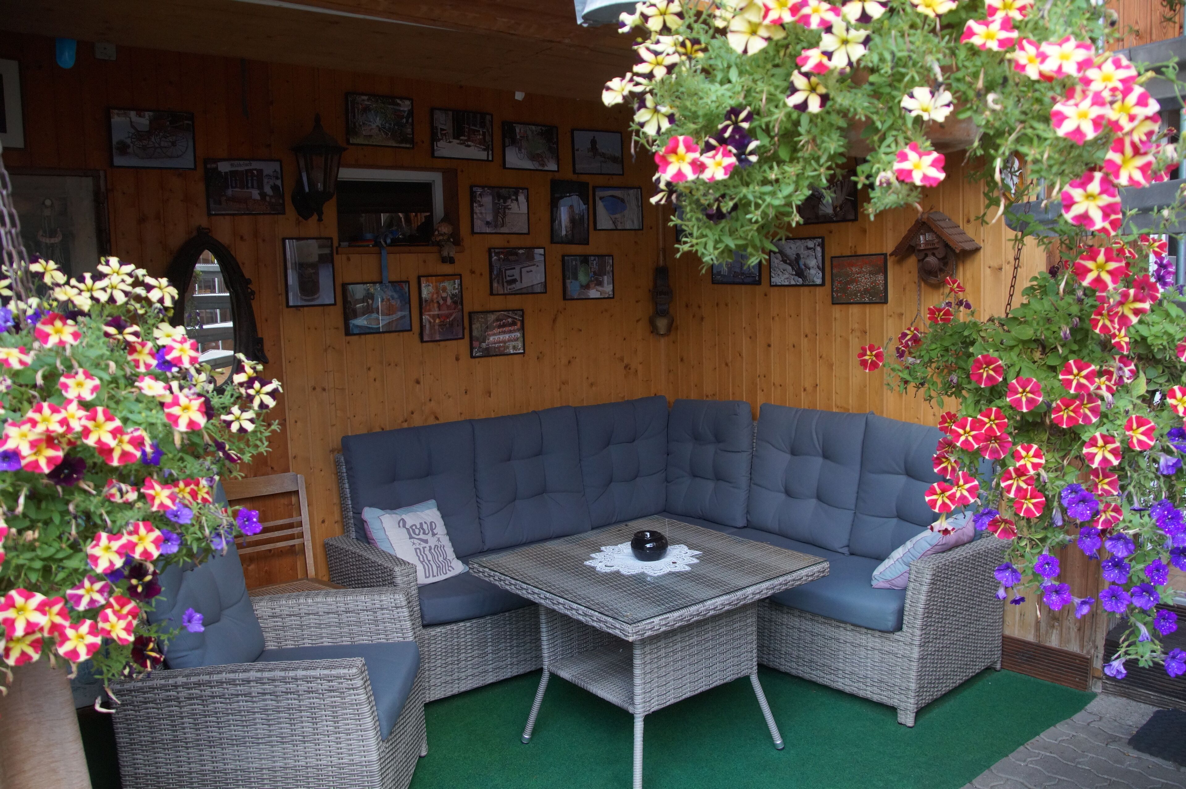 A corner seating area with a cushioned sofa and a small table, surrounded by wicker furniture and vibrant flowers.