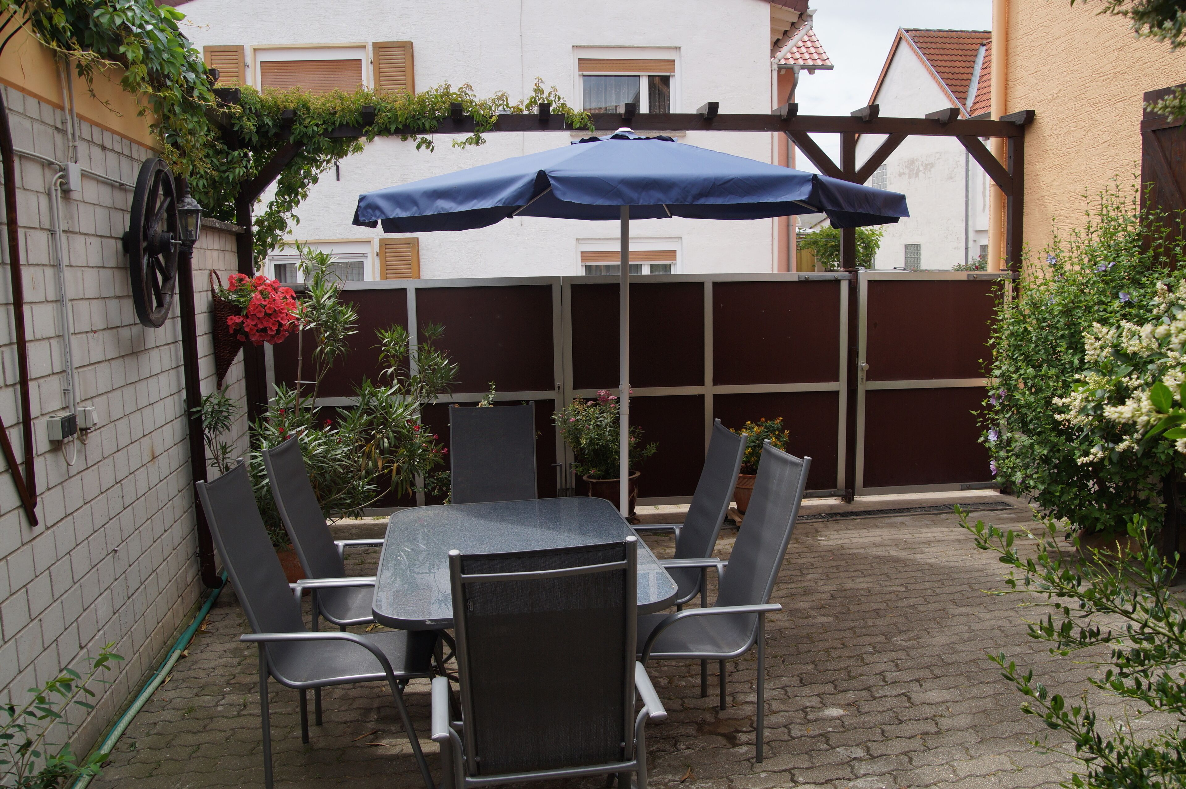 A patio with a table and chairs, a blue umbrella, and a brick wall.