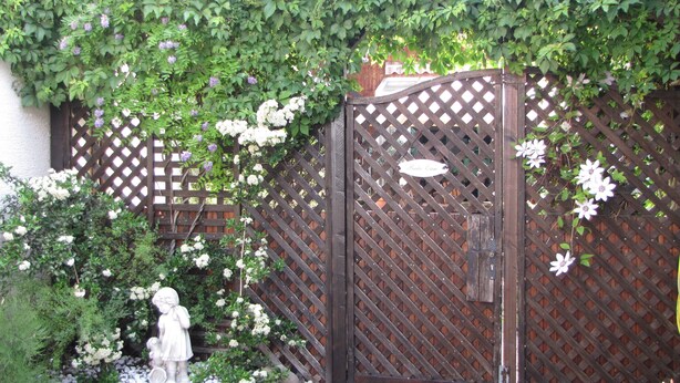 A wooden gate with a lattice design, a white statue, and a variety of flowering plants.