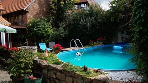 A swimming pool surrounded by stone walls and potted plants, with a small statue and a chair nearby.