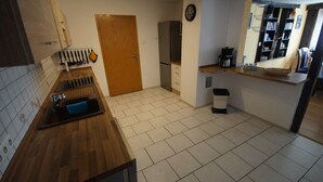 A kitchen with a wooden countertop, a sink, a trash bin, a coffee maker, and a clock on the wall.